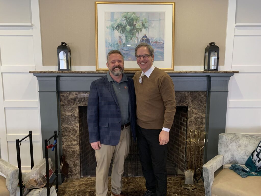 two white males standing in front of a fireplace. Mark Goetz, CEO HomeCare Advocacy Network and Michael Shaw, CEO of White Horse Village
